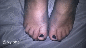 Black nylon pantyhose feet with black nail polish on the bed