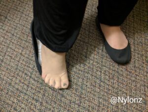 Nude nylon pantyhose feet in flats with black toe nail polish